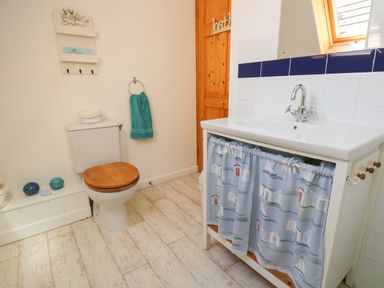 A bathroom with a toilet with wooden seat a sink with a blue patterned curtain and a green towel hanging on a ring at Dartmoor 2 Callington