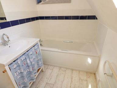 A bathroom with a bathtub a sink with blue curtain and white tiled walls at Dartmoor 2 Callington