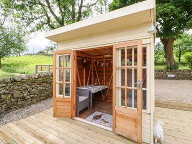 A small wooden shed with open double doors showing a table and chairs inside on a wooden deck at Isaacs Cottage Spartylea near Allendale