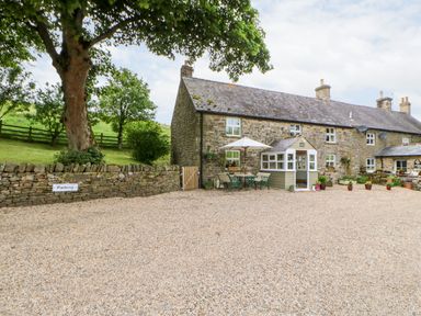 A stone cottage with outdoor seating and potted plants beside a gravel parking area at Isaacs Cottage Spartylea near Allendale