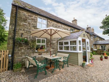 A stone cottage with outdoor seating area and umbrella at Isaacs Cottage Spartylea near Allendale