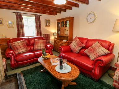 A living room with red leather sofas and plaid cushions at Isaacs Cottage Spartylea near Allendale