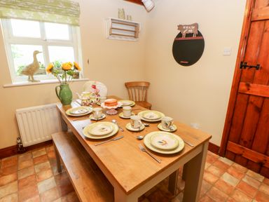 A dining area with a wooden table set with plates cups cutlery and a cake a vase with sunflowers a wooden bench and chair and a window with a duck figurine at Isaacs Cottage in Spartylea near Allendale