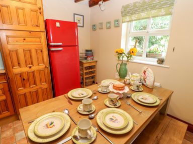 A kitchen dining area with a wooden table set with plates cups and a cake a red fridge and wooden cabinets at Isaacs Cottage Spartylea near Allendale