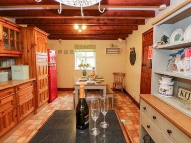 A kitchen with wooden cabinets a red refrigerator a dining table set with dishes and flowers and a counter with a bottle and two glasses at Isaacs Cottage Spartylea near Allendale