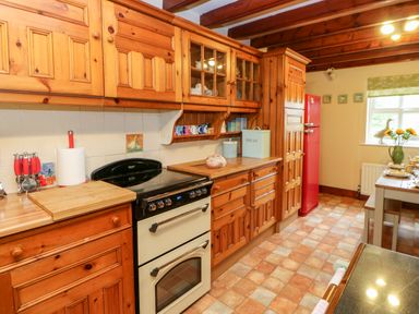 A kitchen with wooden cabinets a black and cream oven a red refrigerator and a dining table near a window at Isaacs Cottage Spartylea near Allendale