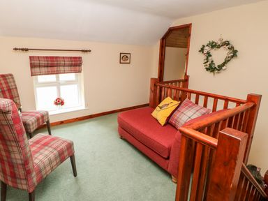 A small sitting area with two plaid chairs, a red sofa, a window with a plaid blind, and wooden stair railing at Isaacs Cottage in Spartylea near Allendale