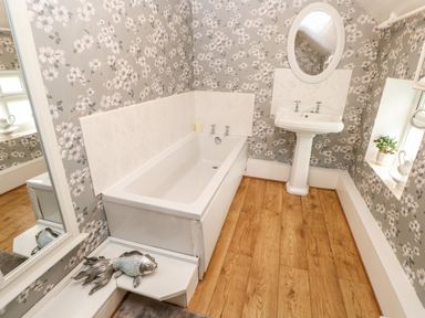 A bathroom with a bathtub sink mirror floral wallpaper and wooden floor at Isaacs Cottage Spartylea near Allendale