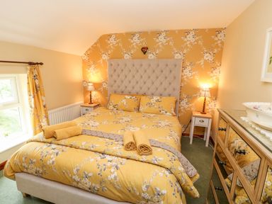 A bedroom with a bed with yellow floral bedding, two bedside tables with lamps, a window with yellow curtains, and a chest of drawers at Isaacs Cottage Spartylea near Allendale