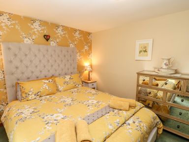 A bedroom with a bed with yellow floral bedding and towels on a mirrored dresser at Isaacs Cottage Spartylea near Allendale