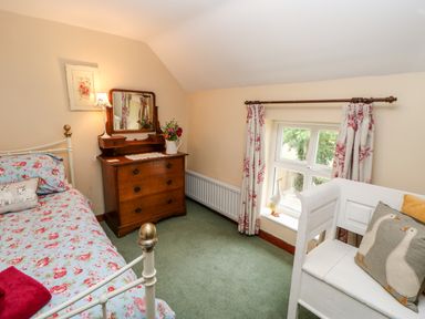 A bedroom with a bed floral bedding wooden dresser with mirror white bench with goose pillows at Isaacs Cottage Spartylea near Allendale