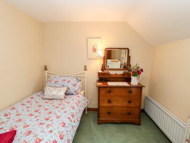 A small bedroom with a single bed with floral bedding and a wooden dresser with a mirror and flowers at Isaacs Cottage Spartylea near Allendale