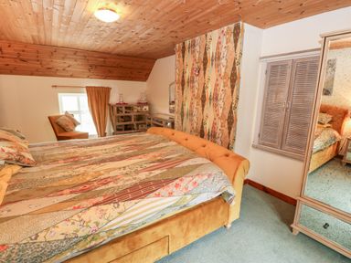 A bedroom with a large bed a mirrored wardrobe a dressing table and an armchair at Isaacs Cottage Spartylea near Allendale