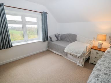 A bedroom with a window a daybed pillows a side table with a lamp and a bed with patterned bedding at West Burnbank in Tarset near Bellingham