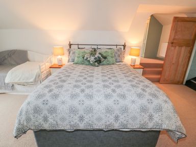 A bedroom with a large bed with patterned bedding and throw pillows lamps on bedside tables and a small daybed with blankets at West Burnbank Tarset near Bellingham