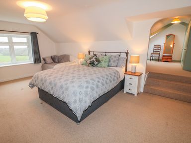 A bedroom with a bed side tables lamps a window with curtains a sofa and an archway leading to another room at West Burnbank in Tarset near Bellingham