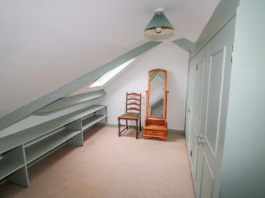 An attic room with built in shelves a wooden chair a free standing mirror and closed cupboards at West Burnbank in Tarset near Bellingham