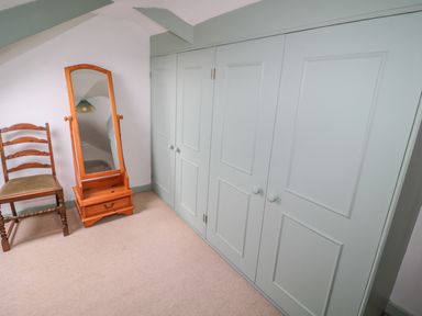 A corner of a room with a wooden chair and a full-length wooden mirror next to pale green built-in cupboards at West Burnbank in Tarset near Bellingham