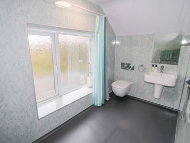A bathroom with a sink a wall-mounted toilet a large window and a shower curtain at West Burnbank in Tarset near Bellingham