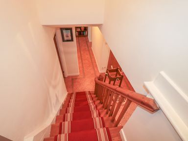 A staircase with a red carpet runner leading down to a hallway with patterned flooring at West Burnbank in Tarset near Bellingham