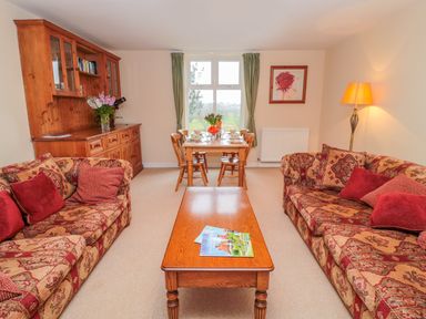 A living room with two patterned sofas red cushions a wooden coffee table and a dining table with chairs at West Burnbank in Tarset near Bellingham