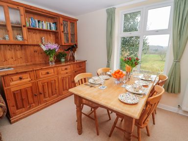 A dining room with a wooden table set with plates and bowls near a window with green curtains at West Burnbank in Tarset near Bellingham