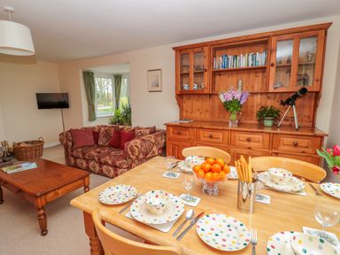 A dining table set with polka dot plates and bowls with a bowl of oranges and breadsticks near a wooden cabinet and a patterned sofa in a living room at West Burnbank in Tarset near Bellingham