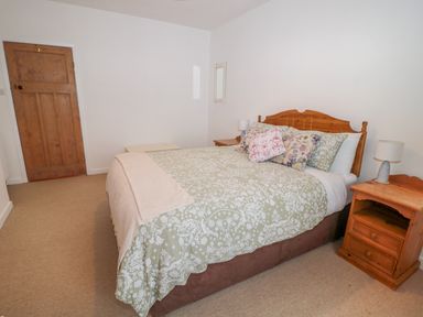 A bedroom with a double bed with floral bedding two wooden nightstands with lamps and a wooden door at West Burnbank in Tarset near Bellingham