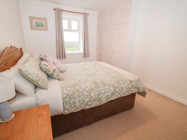A bedroom with a double bed next to a wooden nightstand and a window with curtains at West Burnbank in Tarset near Bellingham