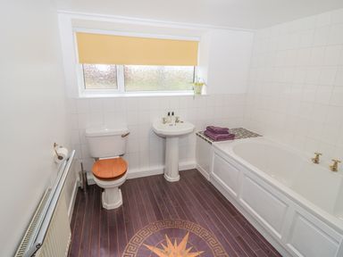 A bathroom with a toilet wooden seat a pedestal sink a bathtub with folded towels on the side window with a blind and wooden floor with a compass design at West Burnbank in Tarset near Bellingham