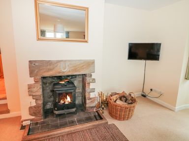 A room with a wood burning stove in a stone fireplace and a wall mounted television at West Burnbank in Tarset near Bellingham