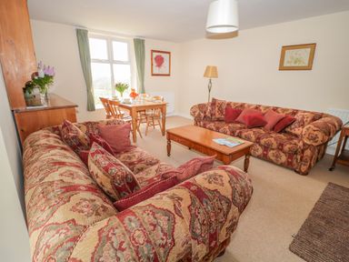 A living room with patterned sofas a wooden coffee table and a dining table with chairs near a window at West Burnbank in Tarset near Bellingham