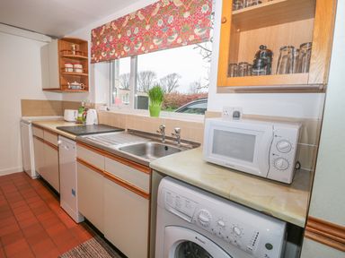 A kitchen with a sink microwave washing machine and window with patterned blind at West Burnbank in Tarset near Bellingham