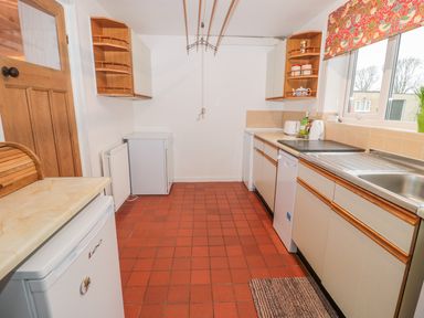 A kitchen with white cabinets a sink a countertop a dishwasher a small refrigerator and a window with patterned blinds at West Burnbank in Tarset near Bellingham