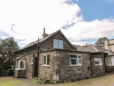 A stone house with multiple windows and a chimney under a partly cloudy sky at West Burnbank in Tarset near Bellingham