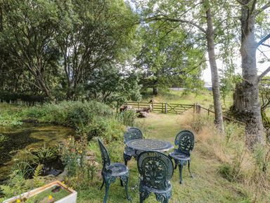A garden area with a metal table and four chairs near a small pond and trees at West Burnbank in Tarset near Bellingham
