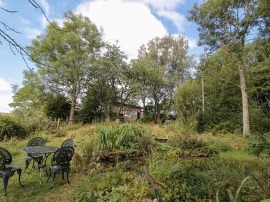 A garden with a metal table and chairs surrounded by trees and plants at West Burnbank Tarset near Bellingham