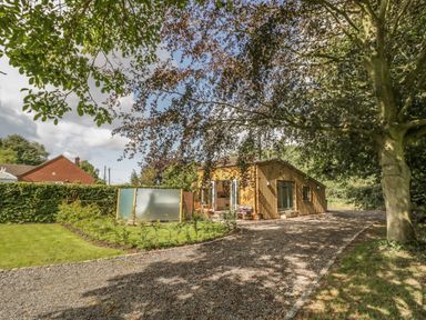 A wooden house with open doors a gravel driveway trees and greenery at Hen House View in Rugeley