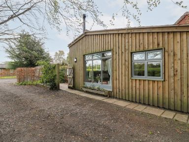 An exterior view of a wooden building with large windows and a gravel pathway at Hen House View in Rugeley