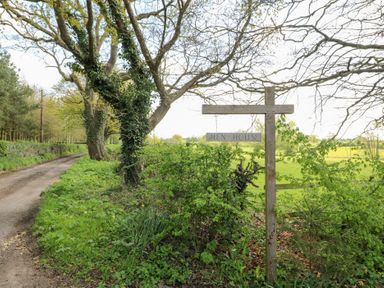 A dirt road beside a tree with a wooden sign that reads Hen House in a rural area at Hen House View in Rugeley