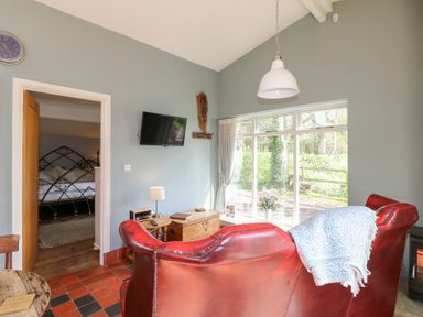A living room with a red leather sofa a mounted television and a door leading to a bedroom at Hen House View in Rugeley