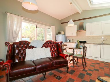 A kitchen with white cabinets a red leather sofa and a small dining table with chairs at Hen House View in Rugeley