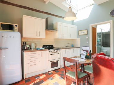 A kitchen with white cabinets a white fridge a stove and a dining table with chairs at Hen House View in Rugeley