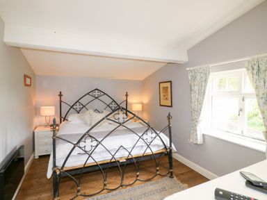 A bedroom with a metal bed frame two bedside tables with lamps a window with floral curtains and wooden floorboards at Hen House View in Rugeley