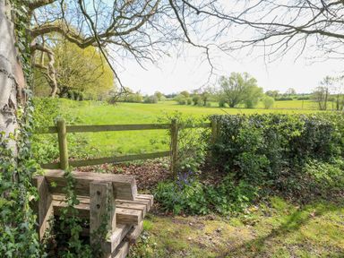 A wooden stile over a fence with a green field and trees in the background at Hen House View in Rugeley