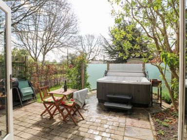 A patio with a hot tub wooden table and chairs with cushions and a bottle on the table at Hen House View in Rugeley