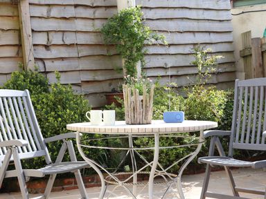 An outdoor patio table with two chairs a plant radio and two mugs in a garden at The Lily Pad in Camborne