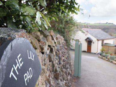 A stone wall with a sign saying The Lily Pad and a driveway leading to a house at The Lily Pad in Camborne