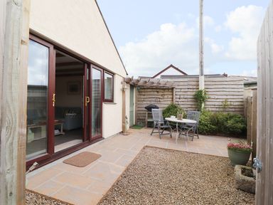 A small patio with a round table and three chairs next to a wooden fence at The Lily Pad in Camborne