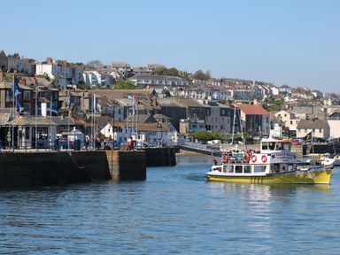 A harbor with a yellow ferry boat and a stone dock with people and buildings on a hillside at The Lily Pad in Camborne